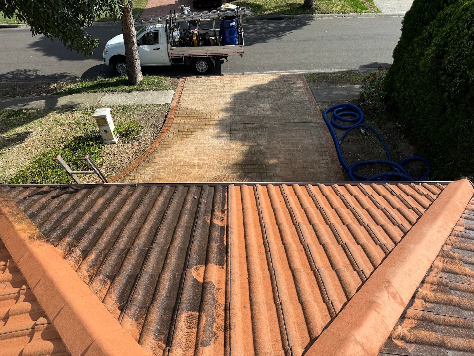 Cleaned terracotta tiled roof with clear gutter lines, work trailer parked in the driveway below