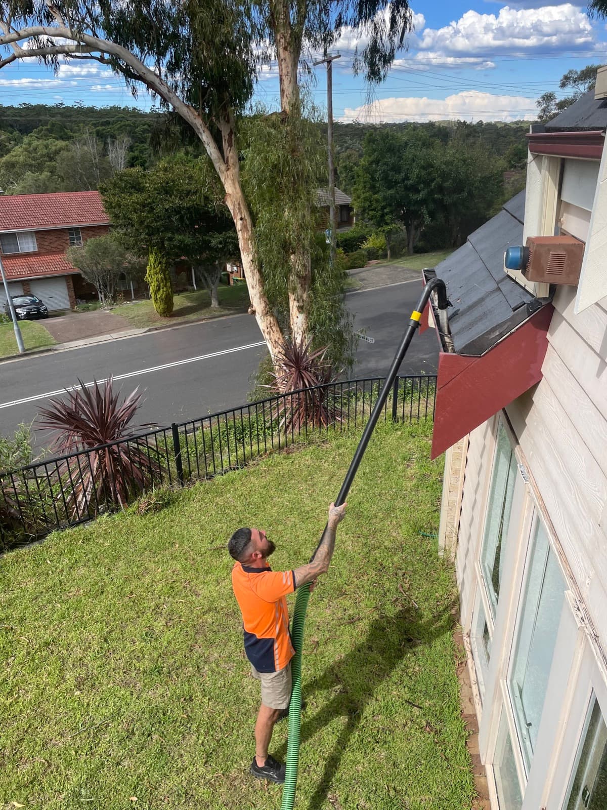 Cameron vacuuming gutters from the ground with a long reach pole, no ladder against the house